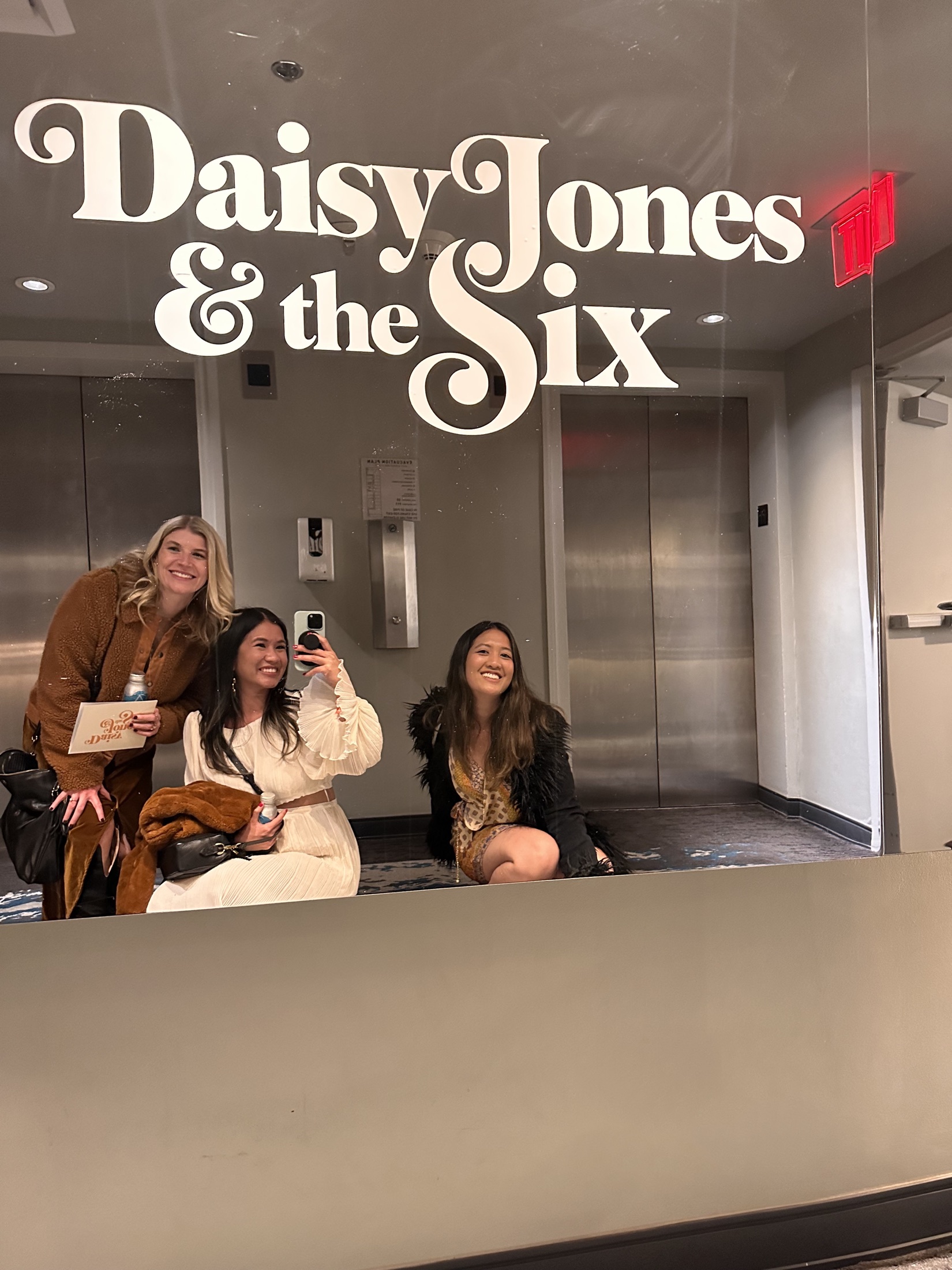 Three team members take a mirror photo beneath the Daisy Jones and the Six logo at the premiere.