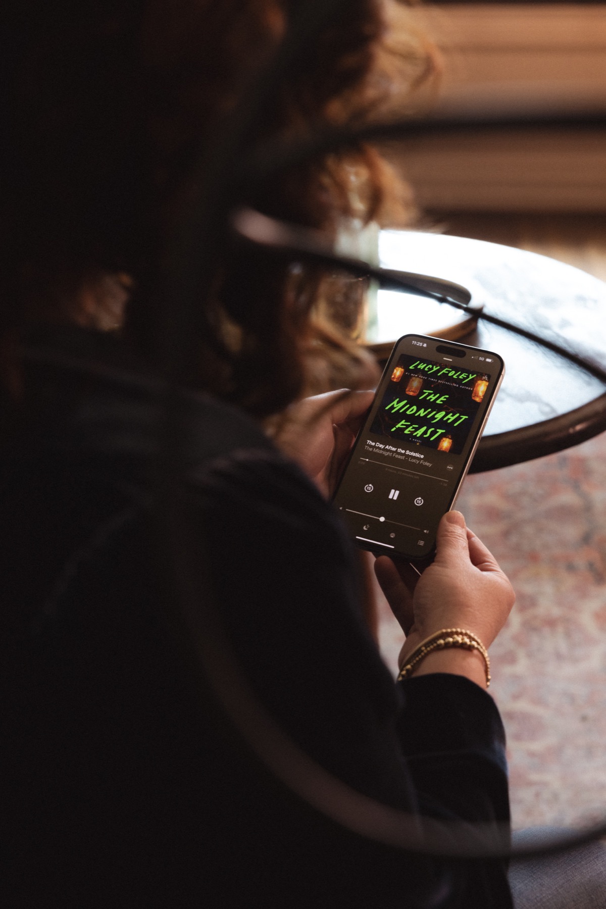 The Midnight Feast playing as an audiobook on a phone held by Ashley Elston.