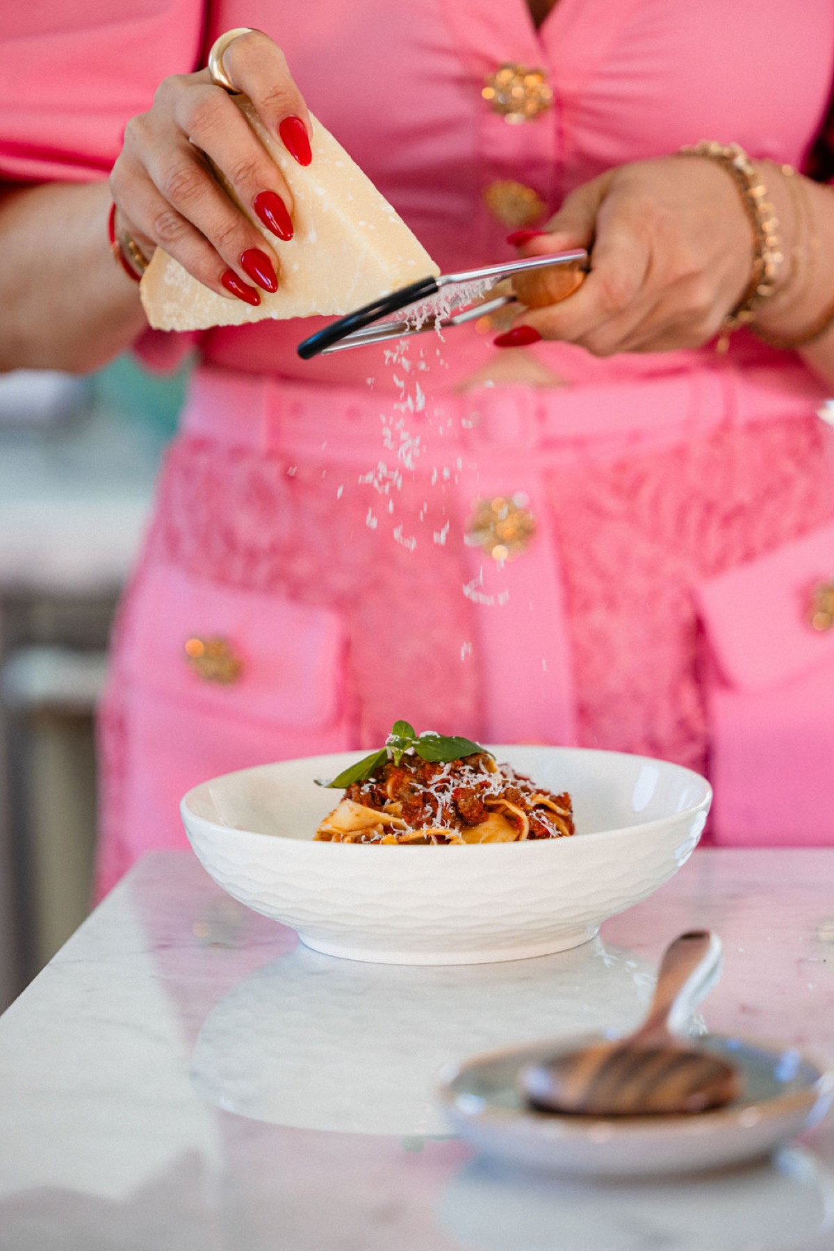Nadia grating cheese over a bowl of pasta.